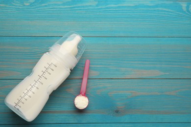 Feeding bottle with infant formula and powder on light blue wooden table, flat lay. Space for text