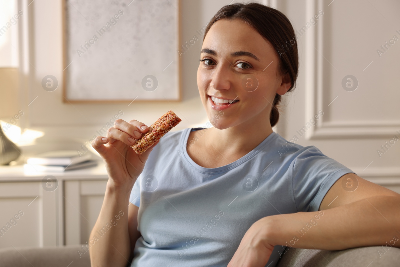 Photo of Woman holding tasty granola bar at home