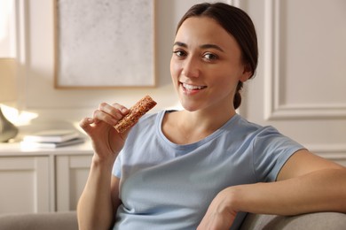 Woman holding tasty granola bar at home