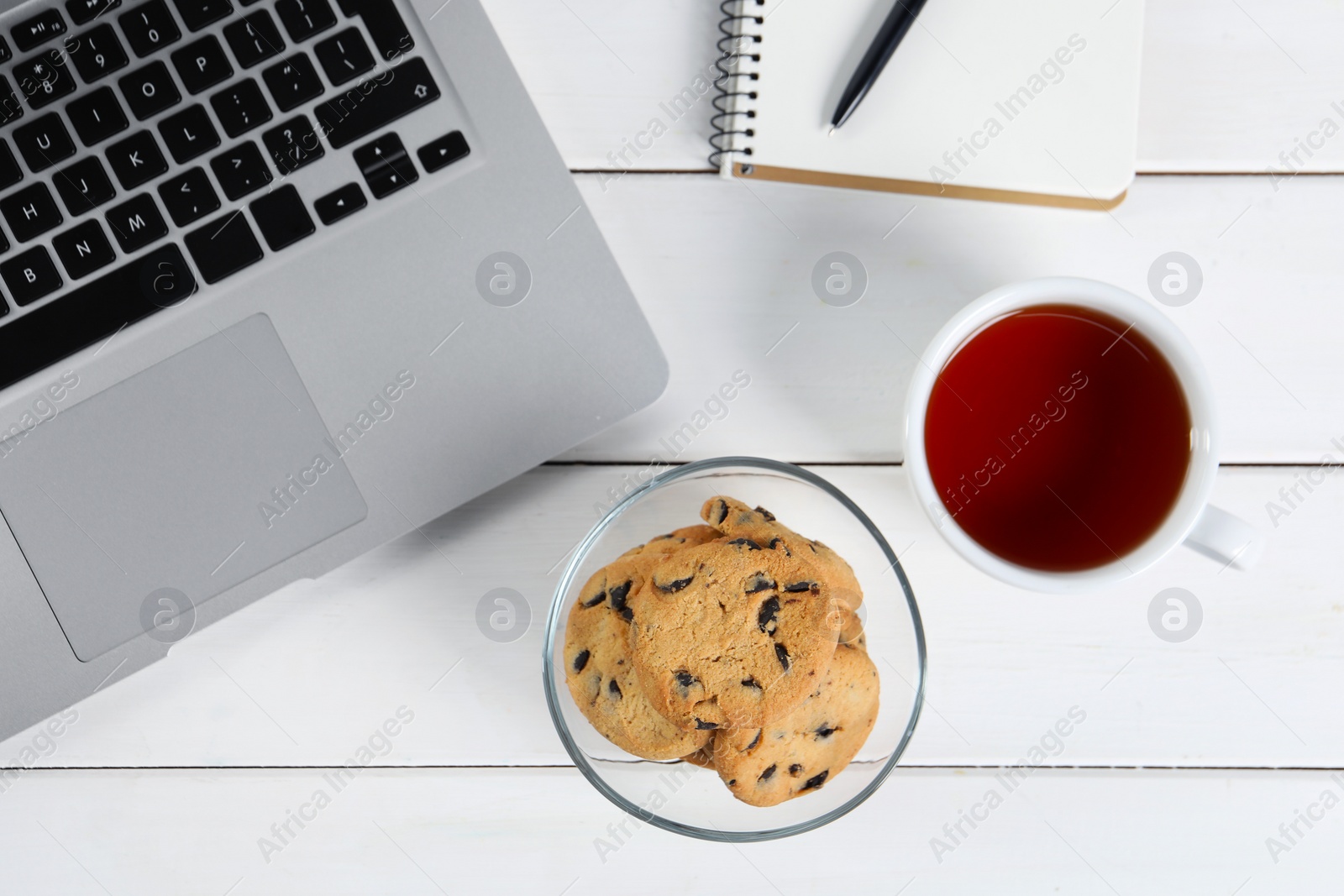 Photo of Chocolate chip cookie, tea and laptop on white wooden table, flat lay