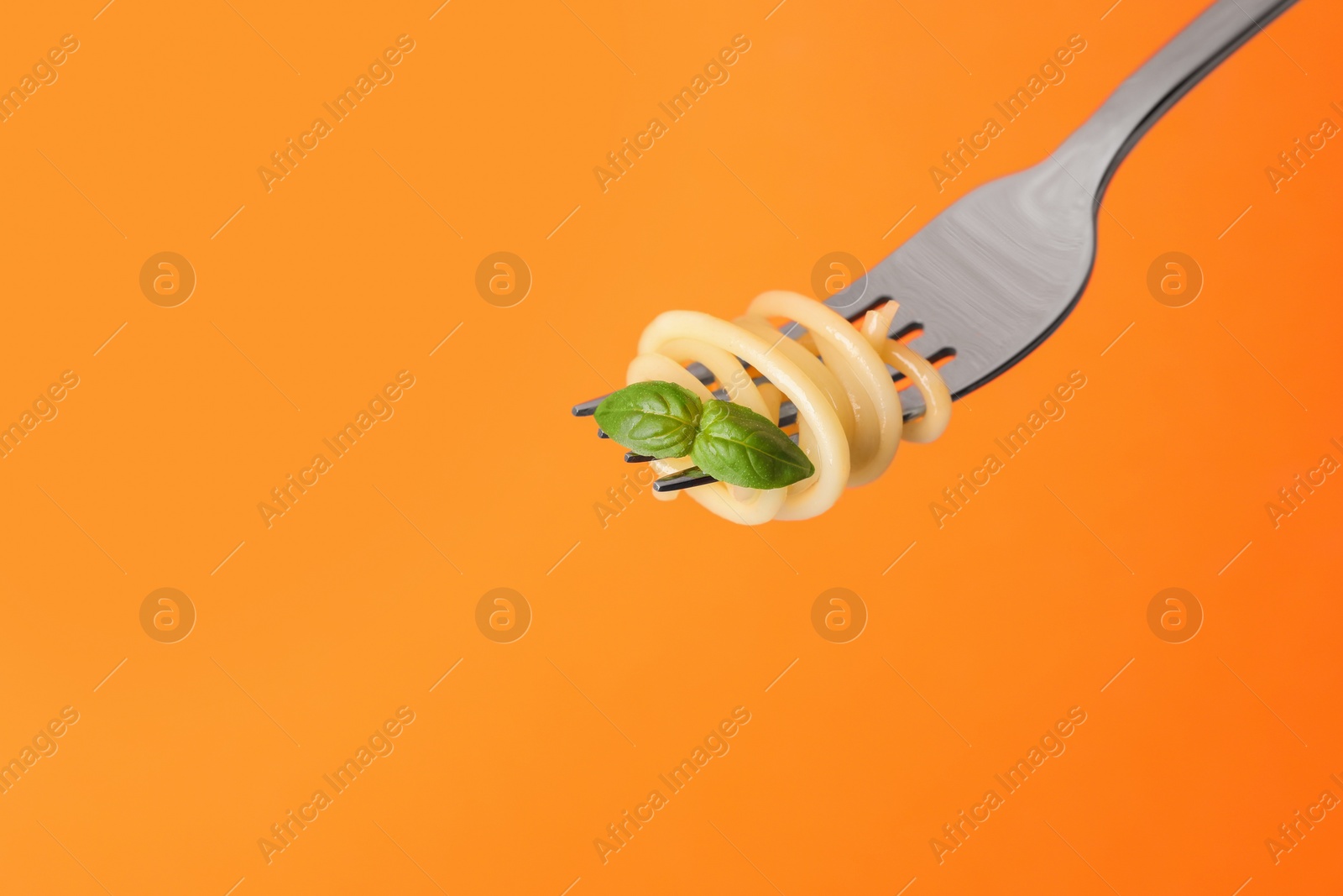 Photo of Fork with tasty pasta and basil on orange background, space for text