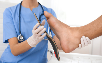 Female orthopedist fitting insole on patient's foot in clinic, closeup