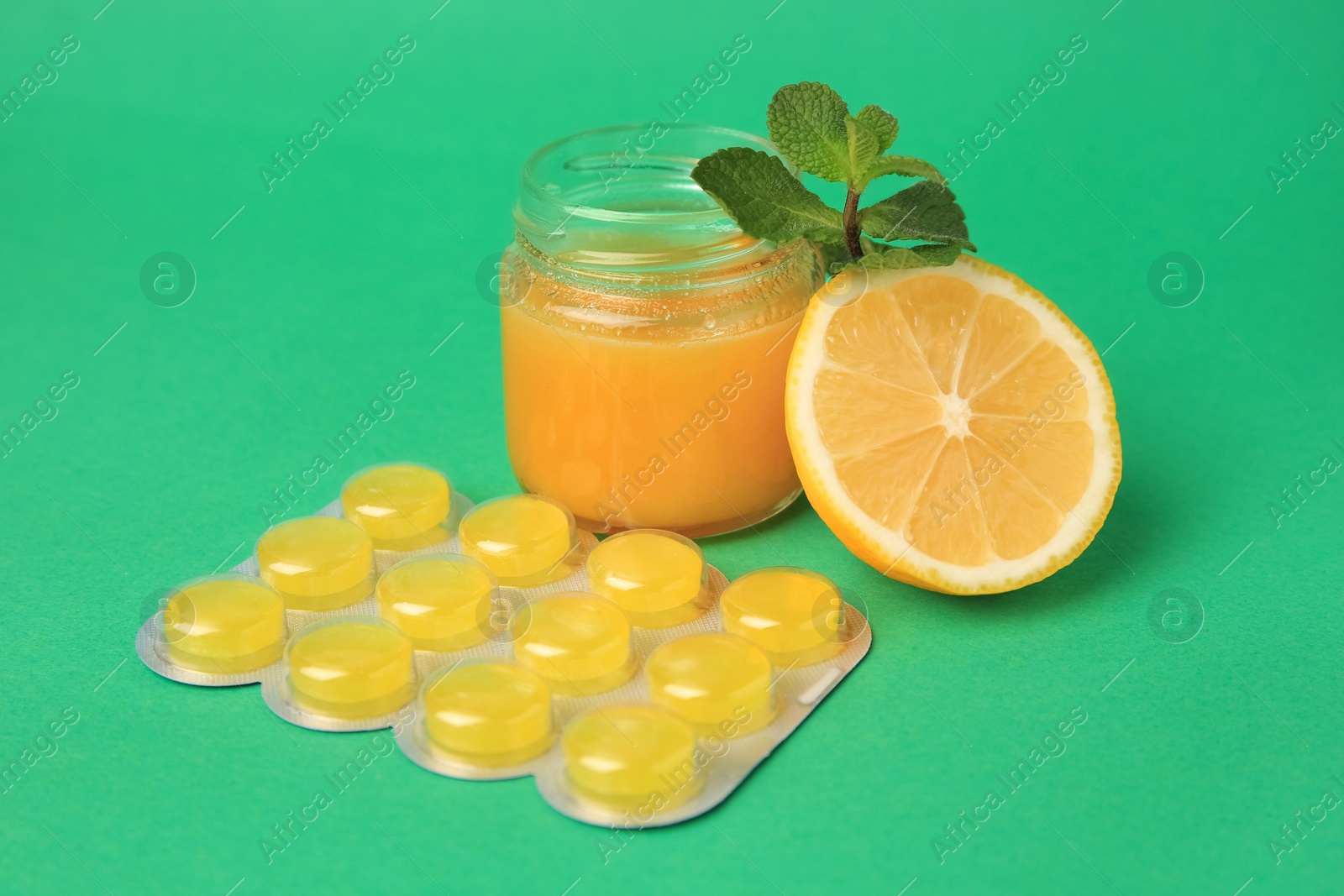 Photo of Jar of honey, fresh lemon, mint leaves and blister with cough drops on green background