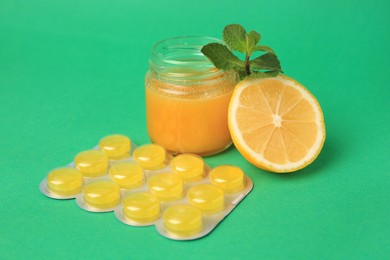 Photo of Jar of honey, fresh lemon, mint leaves and blister with cough drops on green background