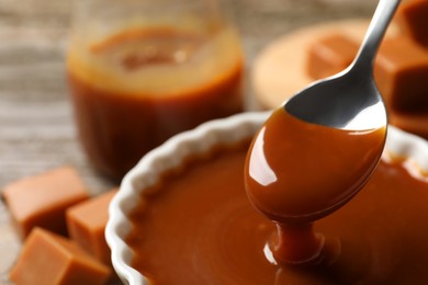 Taking tasty salted caramel with spoon from bowl at table, closeup
