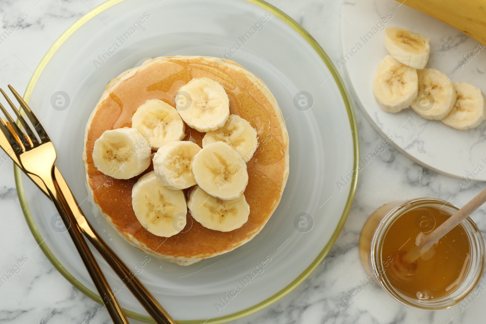 Photo of Delicious pancakes with bananas and honey served on white marble table, flat lay