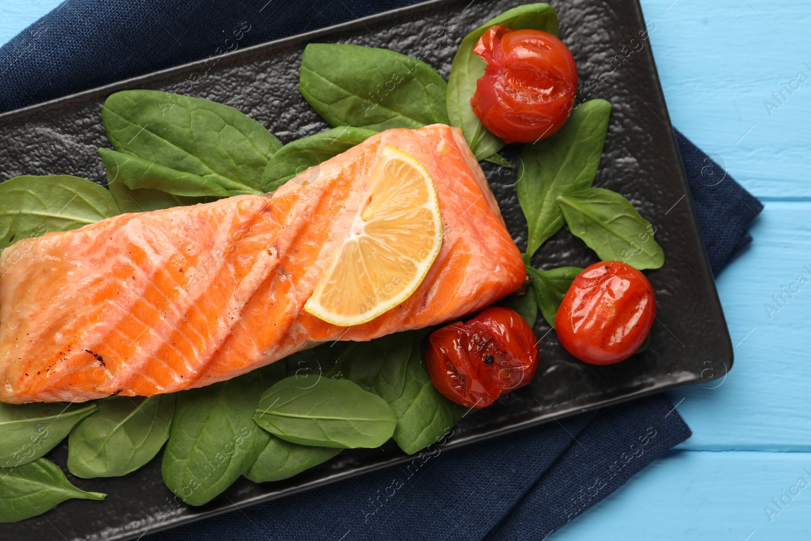Photo of Tasty grilled salmon with tomatoes, spinach and lemon on light blue table, top view
