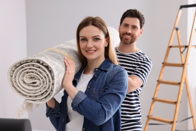 Smiling couple holding rolled carpet in room