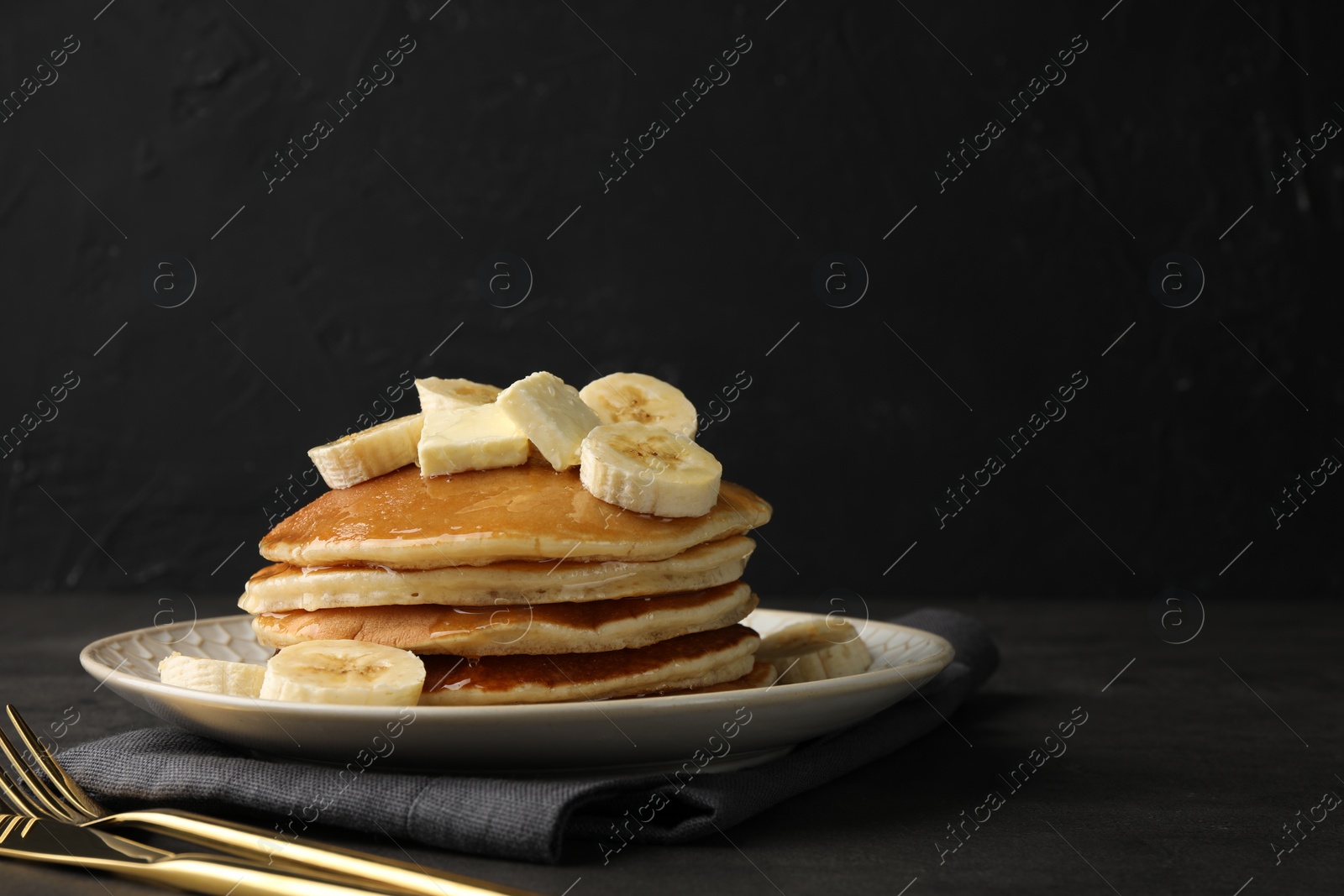 Photo of Delicious pancakes with bananas, butter and honey on dark table. Space for text