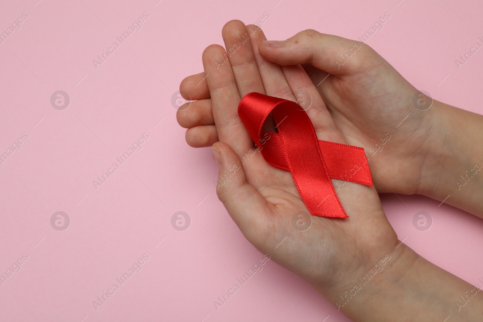 Photo of Little girl holding red ribbon on pink background, closeup with space for text. AIDS disease awareness