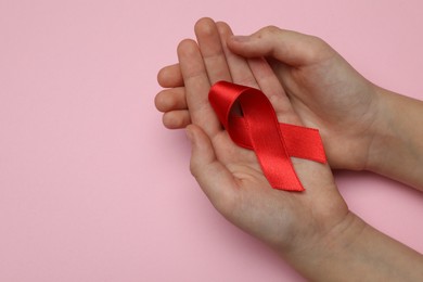 Photo of Little girl holding red ribbon on pink background, closeup with space for text. AIDS disease awareness