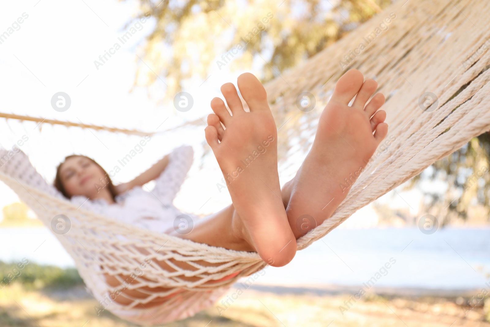 Photo of Young woman relaxing in hammock on beach, focus on legs. Summer vacation