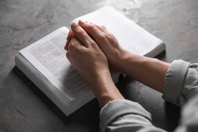 Photo of Religion. Christian woman praying over Bible at gray table, closeup