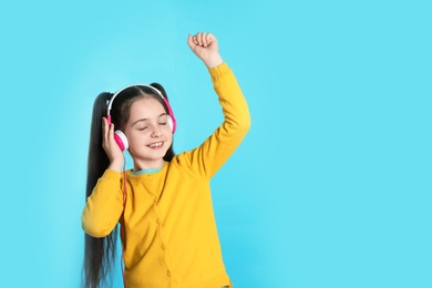 Cute girl enjoying music in headphones on color background. Space for text