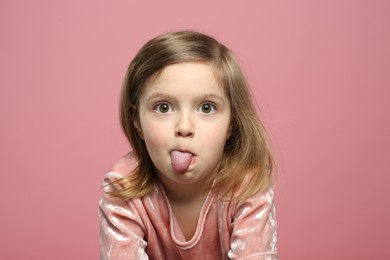 Photo of Funny little girl showing her tongue on pink background