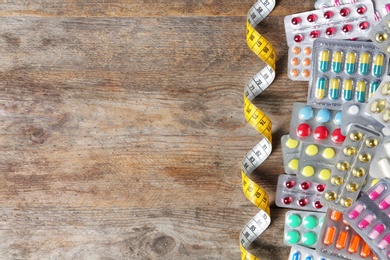 Weight loss pills in blister packs and measuring tape on wooden background, top view. Space for text