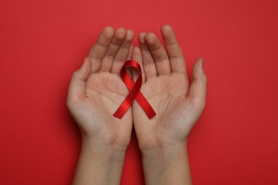 Photo of Little girl holding red ribbon on bright background, top view. AIDS disease awareness