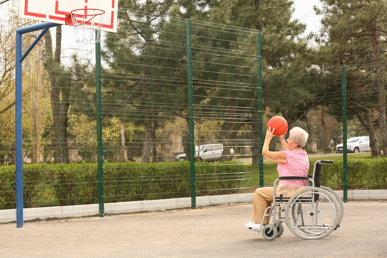 Photo of Senior woman in wheelchair playing basketball on sports ground