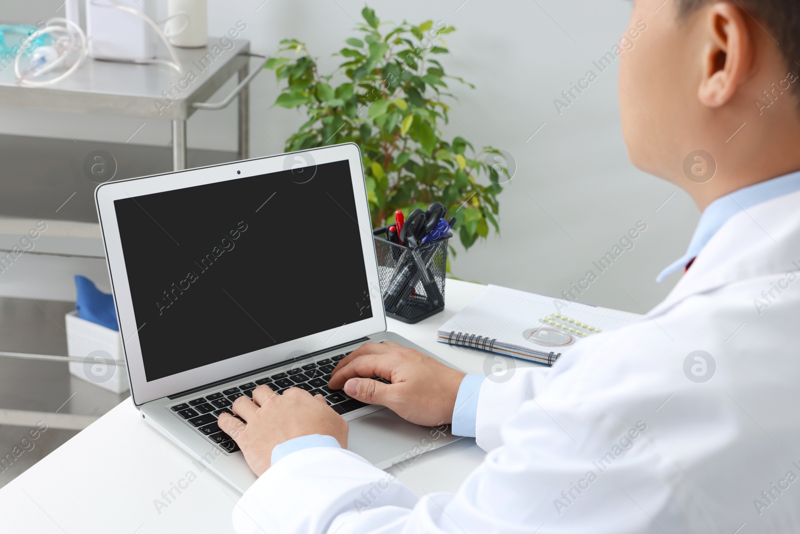 Photo of Doctor working with laptop at white desk in clinic. Online medicine