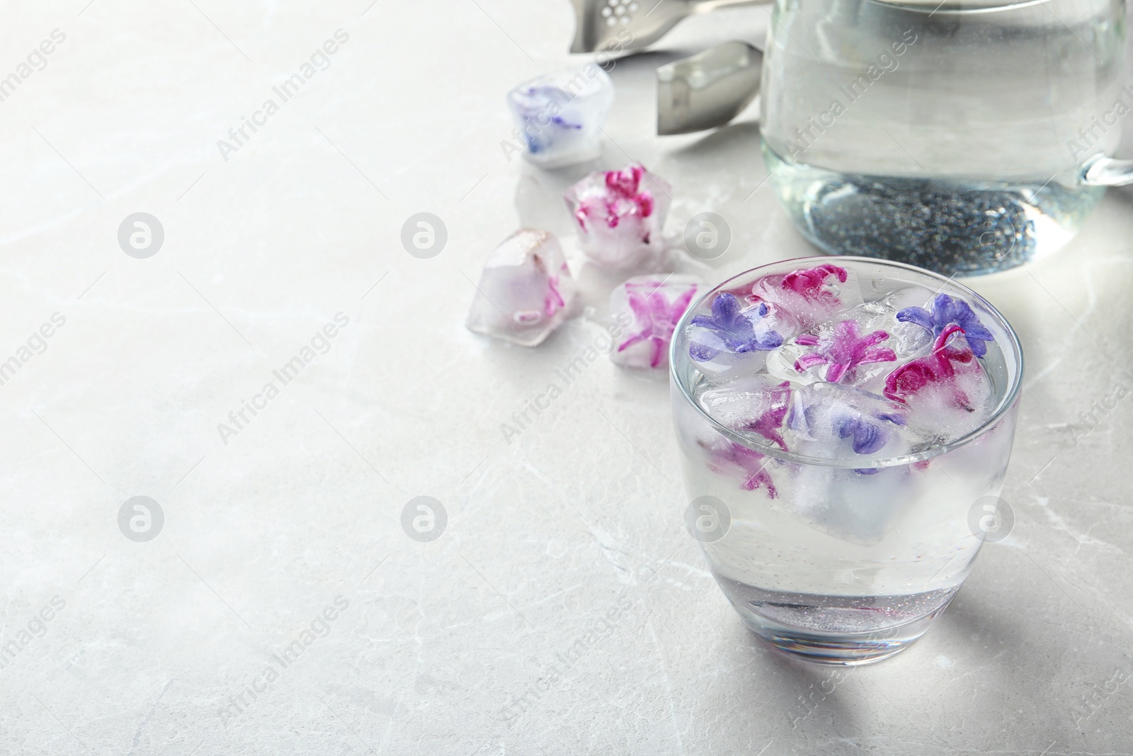 Photo of Glass of water with floral ice cubes on table. Space for text