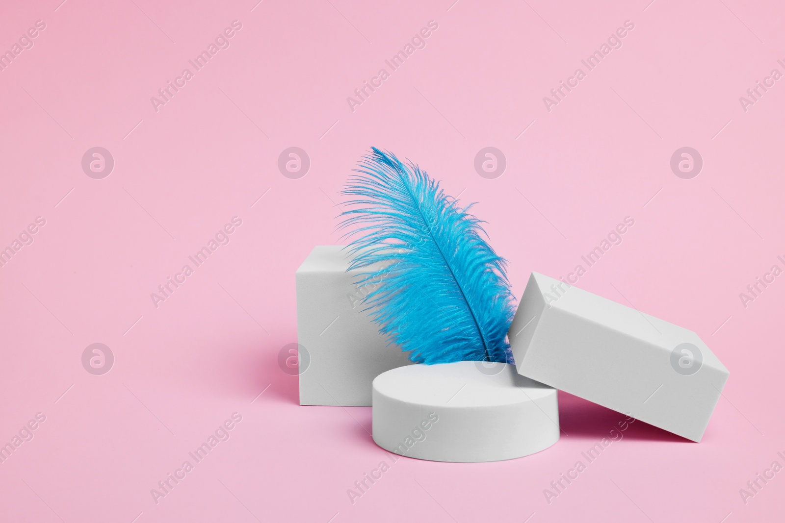Photo of Scene for product presentation. Podiums of different geometric shapes and decorative feather on pink background, space for text