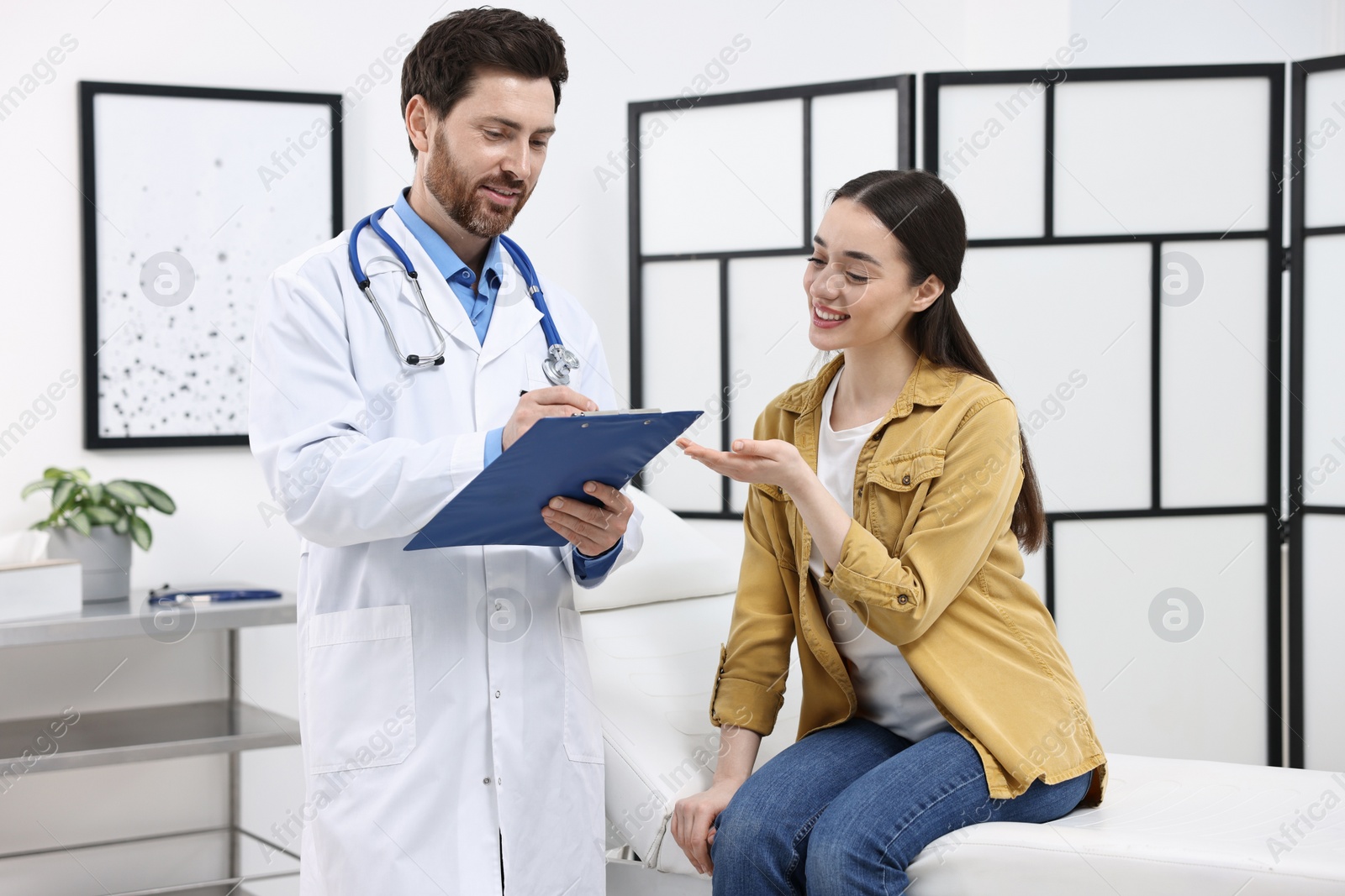 Photo of Doctor with clipboard consulting patient during appointment in clinic