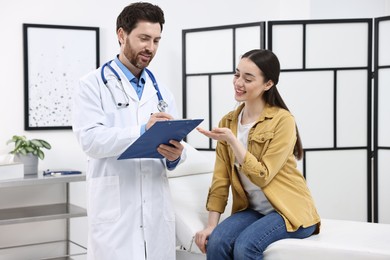 Photo of Doctor with clipboard consulting patient during appointment in clinic