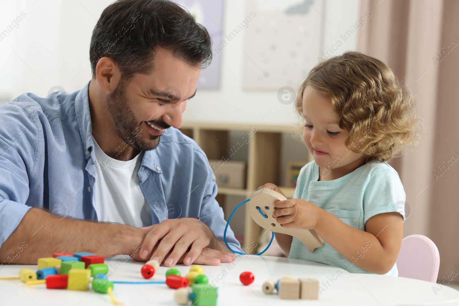 Photo of Motor skills development. Father and daughter playing with wooden lacing toy at table indoors