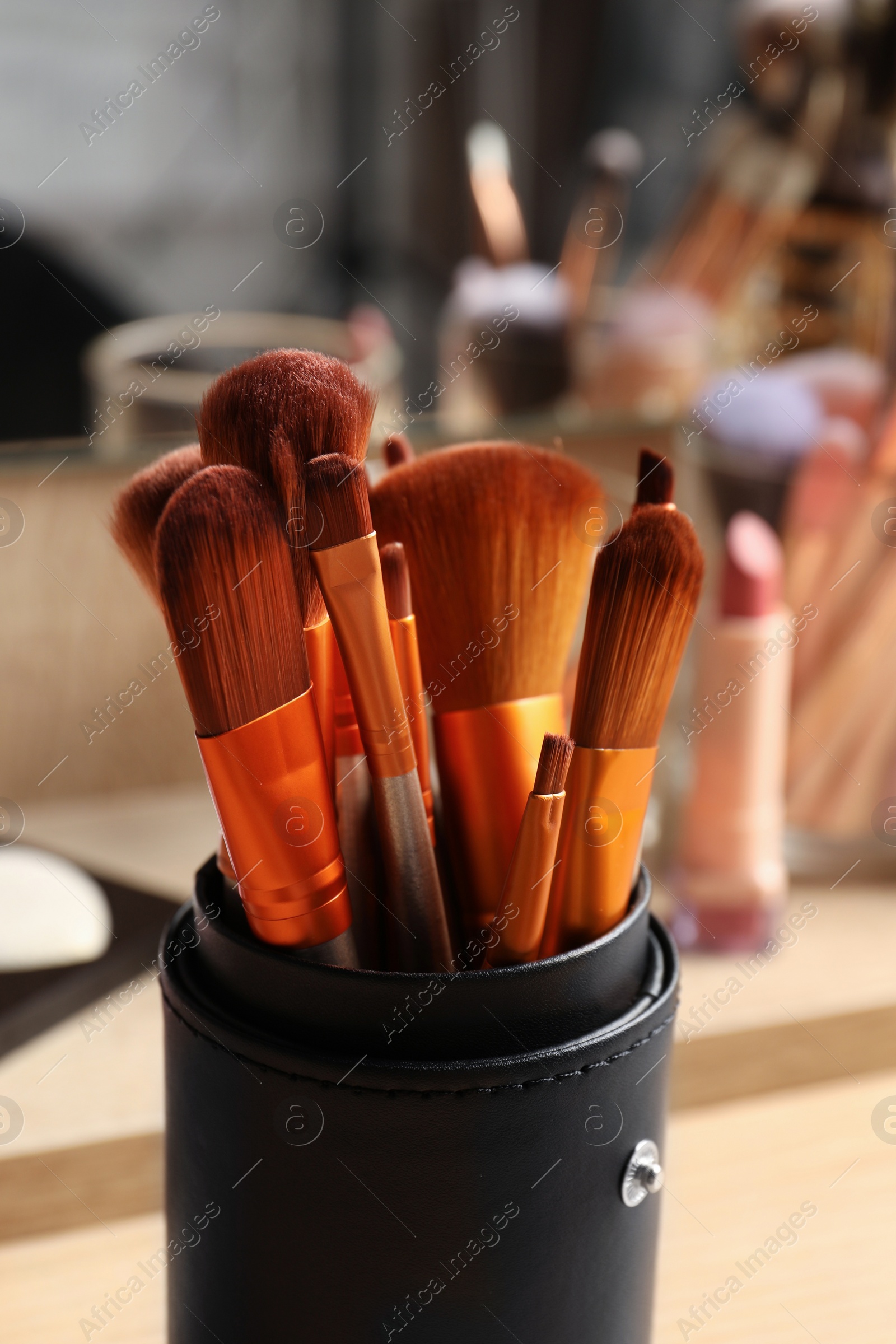 Photo of Set of professional brushes and makeup products near mirror on wooden table, closeup