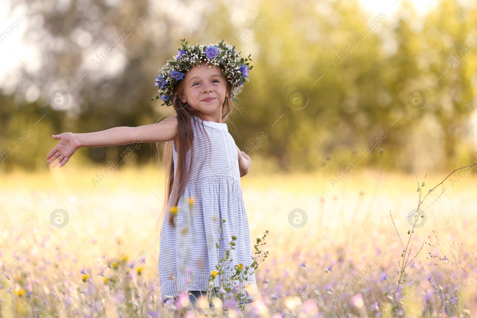 Photo of Cute little girl wearing flower wreath outdoors, space for text. Child spending time in nature