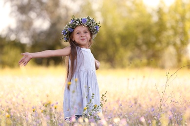 Cute little girl wearing flower wreath outdoors, space for text. Child spending time in nature