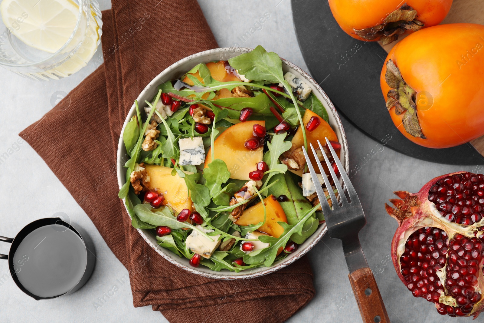 Photo of Tasty salad with persimmon, blue cheese, pomegranate and walnuts served on light grey table, flat lay