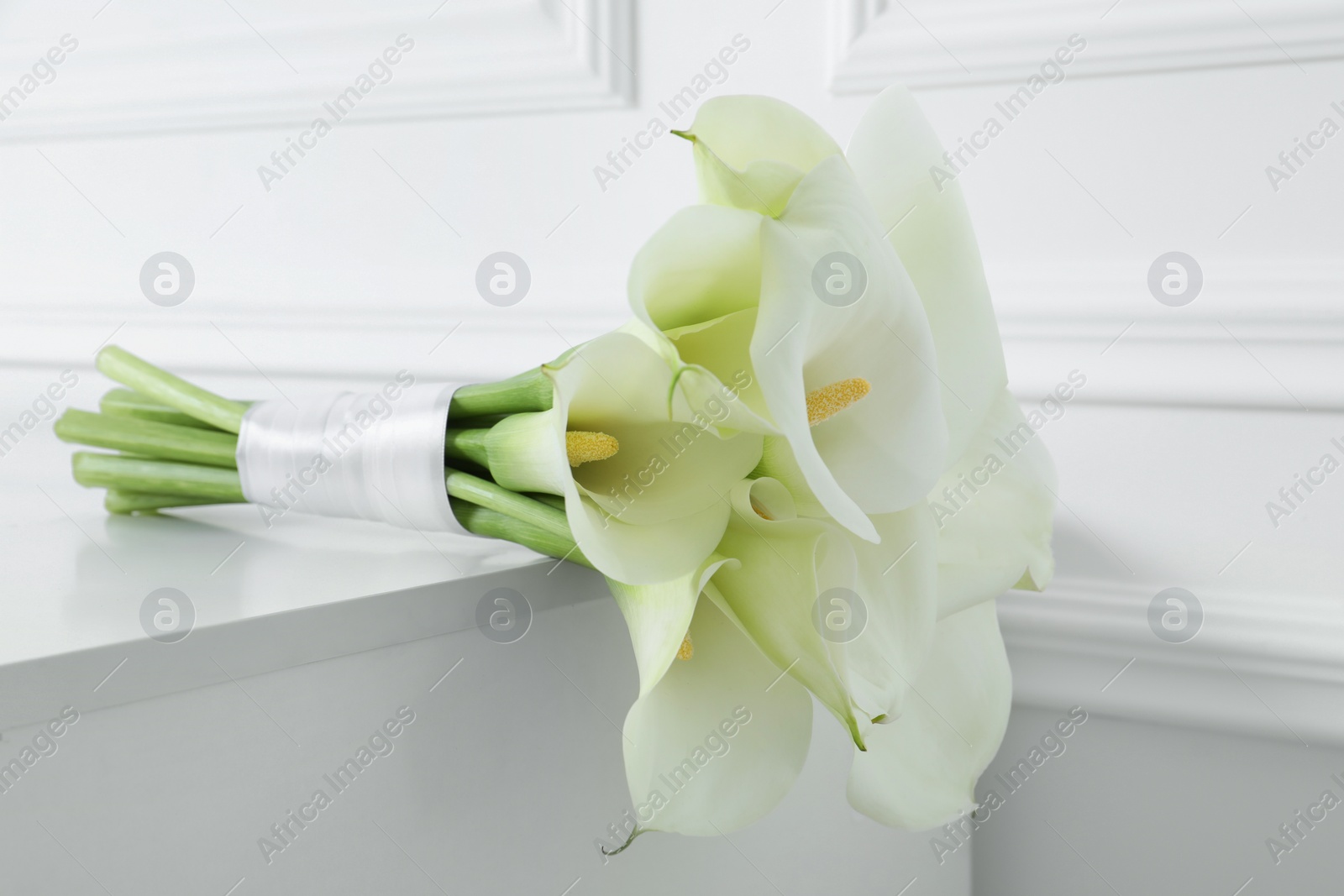 Photo of Beautiful calla lily flowers tied with ribbon on white table, closeup