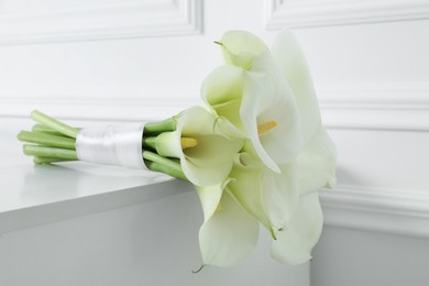 Beautiful calla lily flowers tied with ribbon on white table, closeup