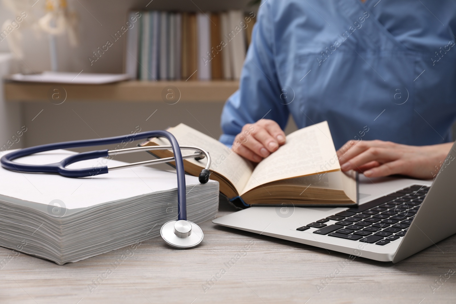 Photo of Woman with book, stethoscope and laptop at table indoors, closeup. Medical education