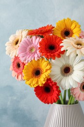 Photo of Bouquet of beautiful colorful gerbera flowers in vase on blue background