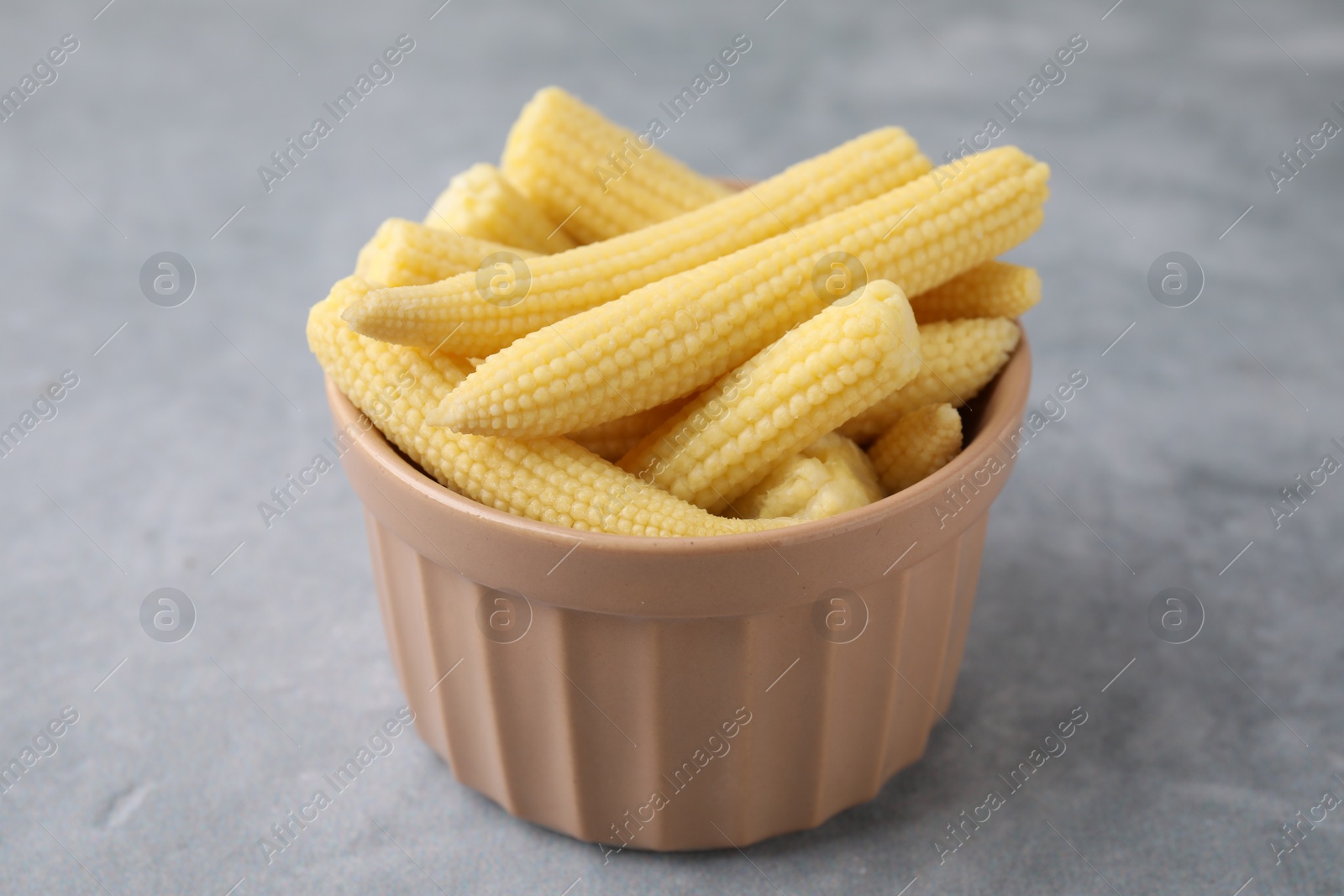 Photo of Tasty fresh yellow baby corns in bowl on grey table, closeup