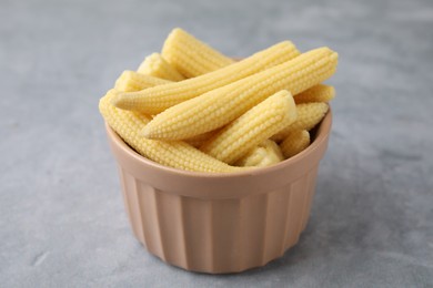 Tasty fresh yellow baby corns in bowl on grey table, closeup