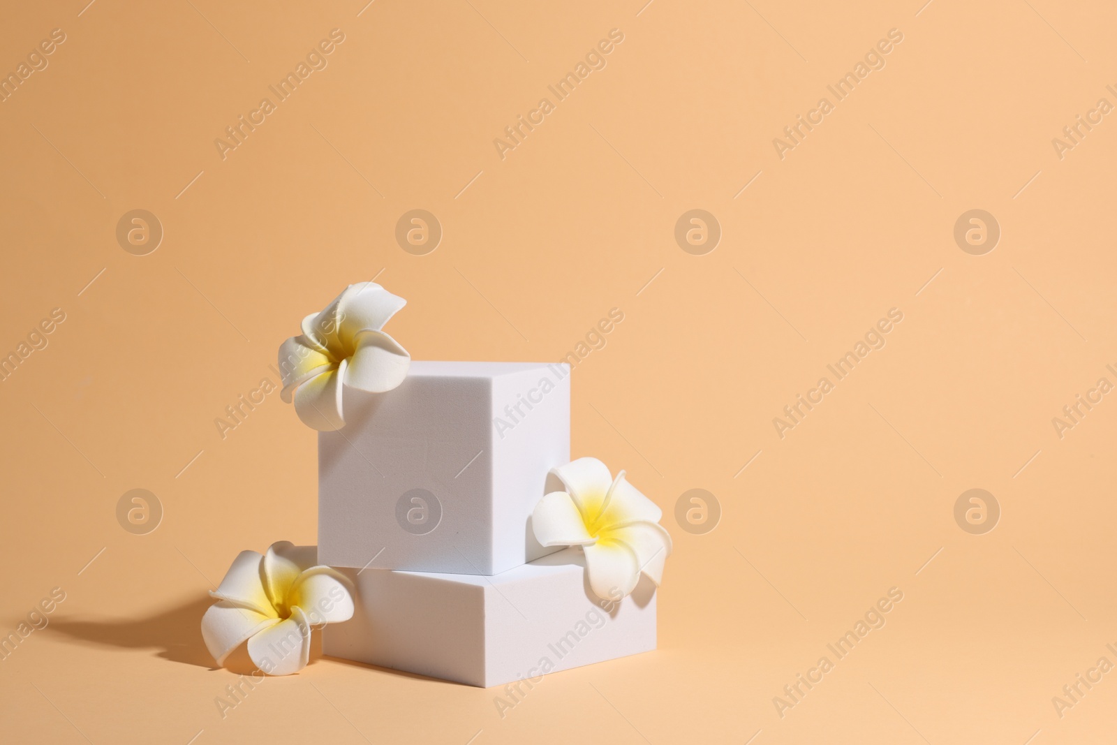 Photo of Scene with podium for product presentation. Figures of different geometric shapes and flowers on pale orange background, space for text