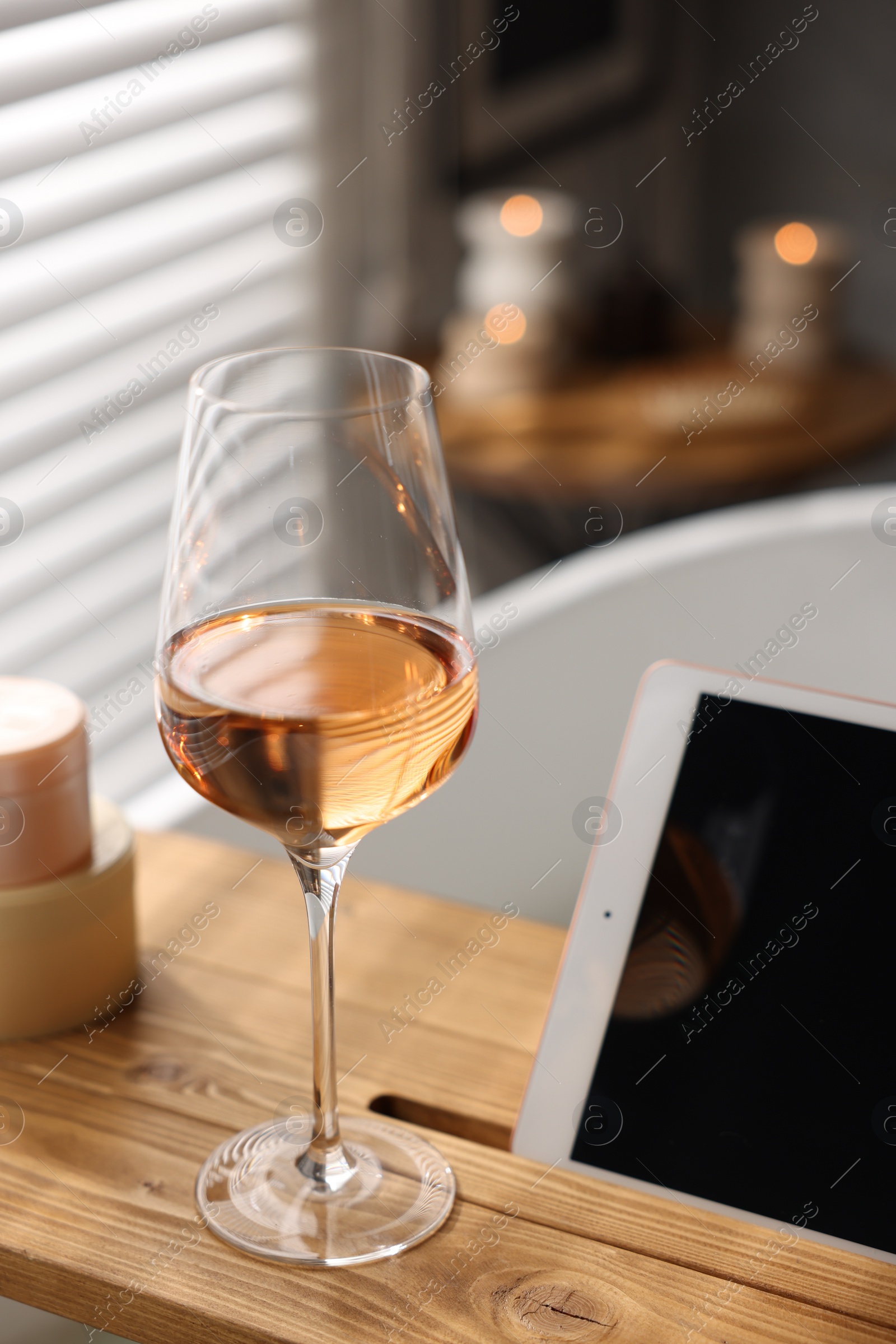 Photo of Wooden tray with tablet and wine on bathtub in bathroom