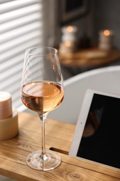 Photo of Wooden tray with tablet and wine on bathtub in bathroom