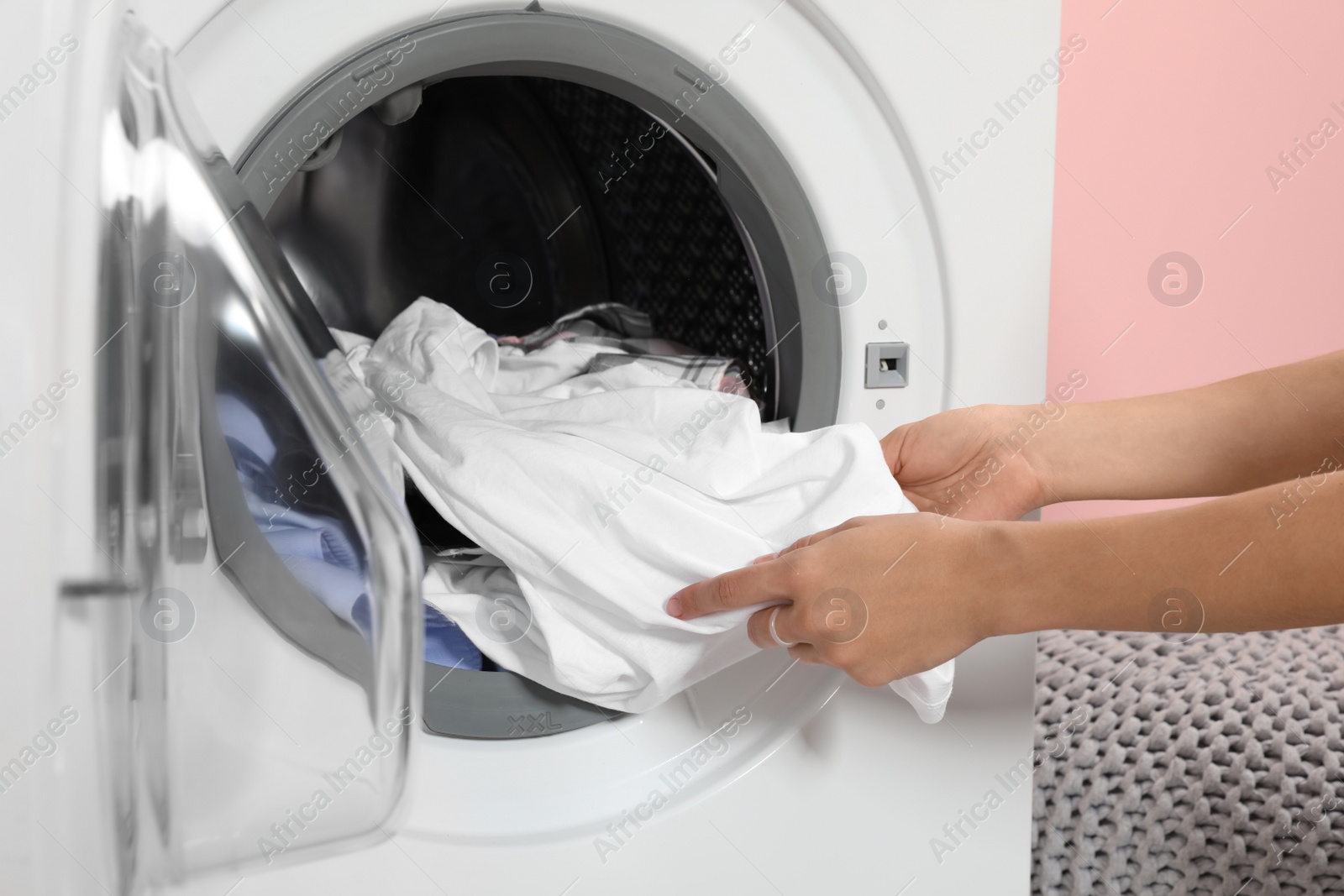 Photo of Woman taking laundry out of washing machine indoors, closeup