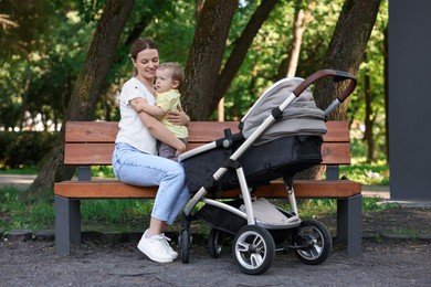 Happy nanny with cute little boy on bench in park