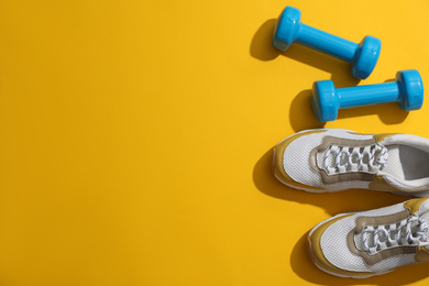 Photo of Dumbbells, sneakers and space for text on yellow background, flat lay. Physical fitness