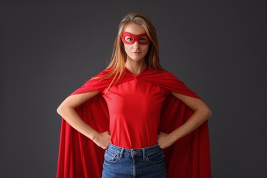 Photo of Confident woman wearing superhero cape and mask on grey background