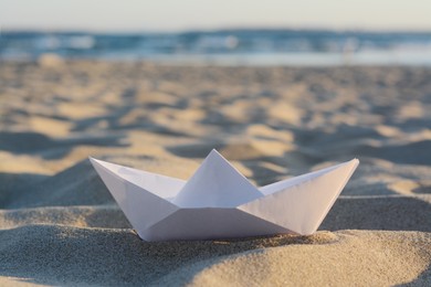 Photo of Beautiful white paper boat on sand outdoors, closeup