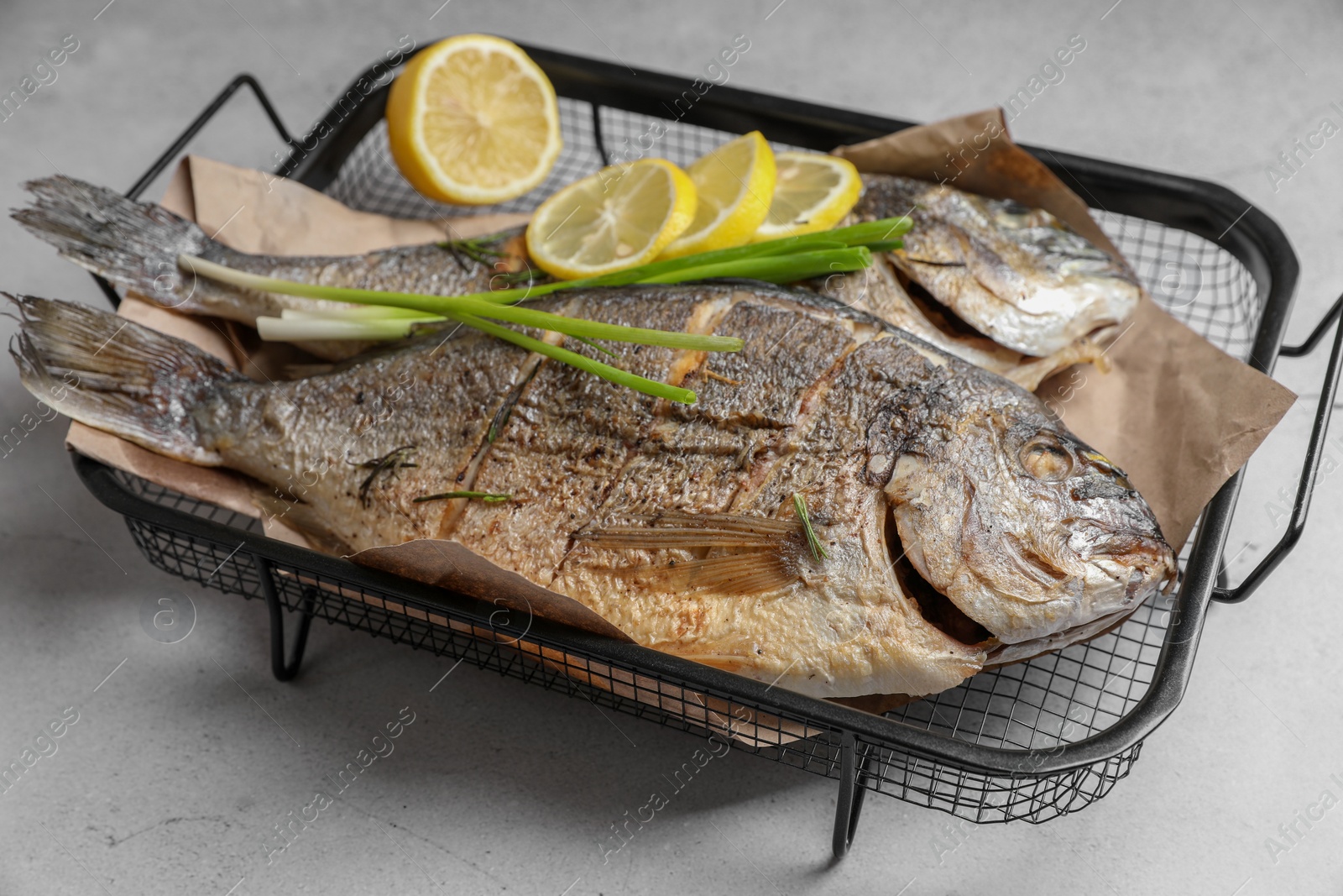 Photo of Seafood. Delicious baked fish served with green onion and lemon on light textured table, closeup