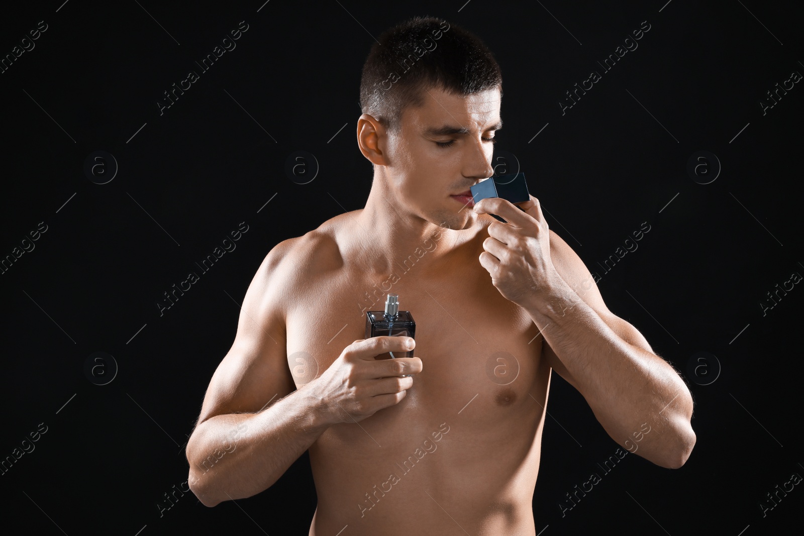 Photo of Handsome young man smelling perfume on black background