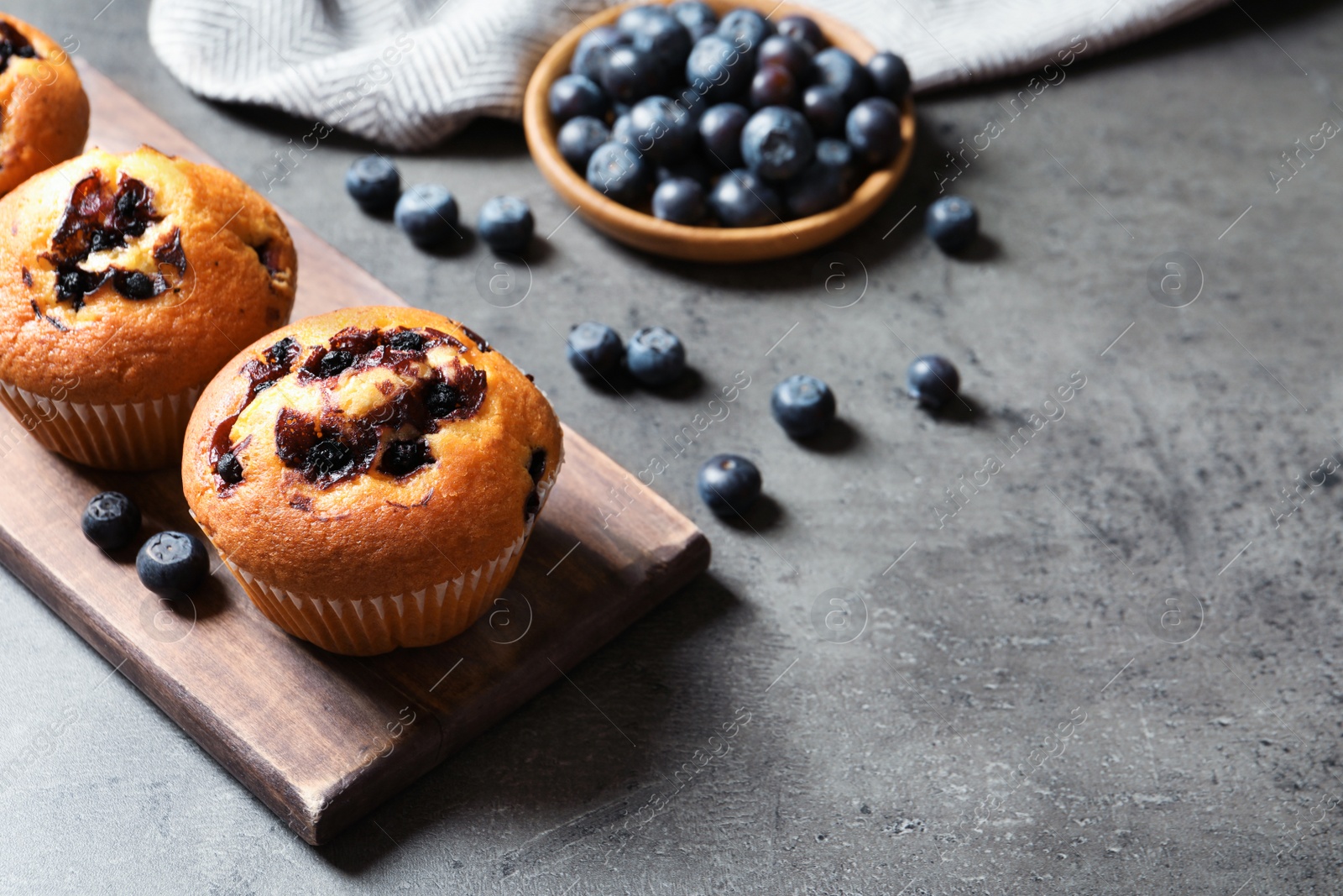 Photo of Wooden board with blueberry muffins on grey table, space for text