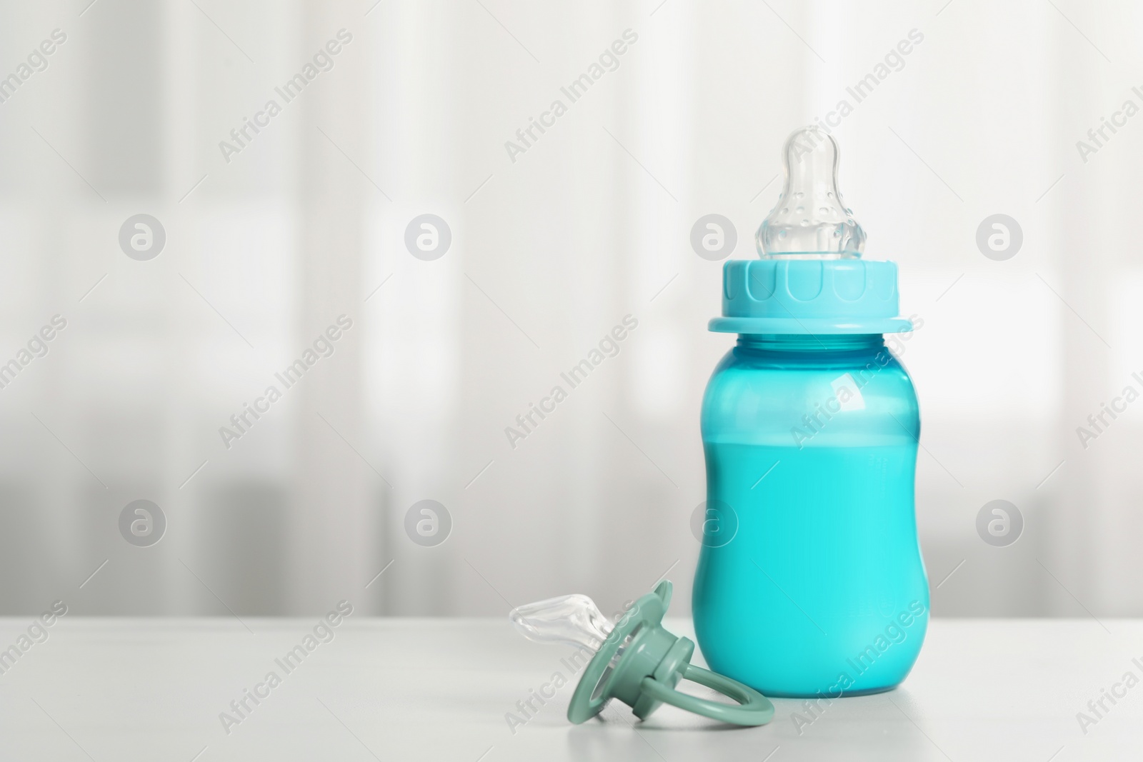Photo of Feeding bottle with milk and pacifier on white table indoors, space for text
